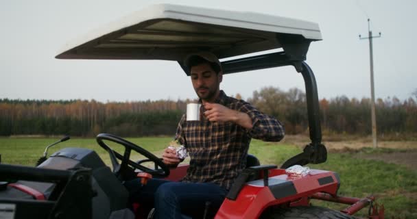 Joven agricultor comiendo sándwich sentado en la cabina abierta de la máquina agrícola — Vídeo de stock