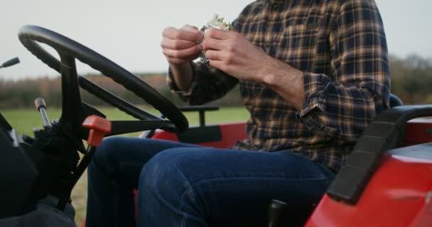 Joven agricultor comiendo sándwich sentado en la cabina abierta de la máquina agrícola — Vídeo de stock