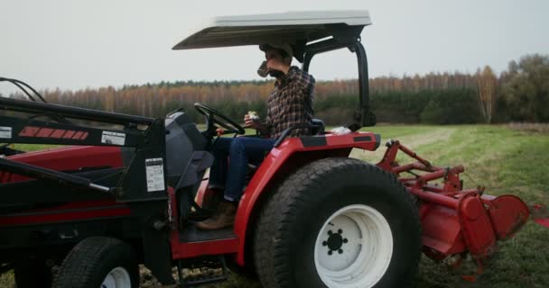 Young farmer eating sandwich sitting in the open cabin of agricultural machine — Stock Video