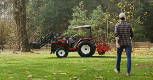 En ung man kliver in i en traktor och gör sig redo att arbeta ute på fältet på höstdagen. — Stockvideo