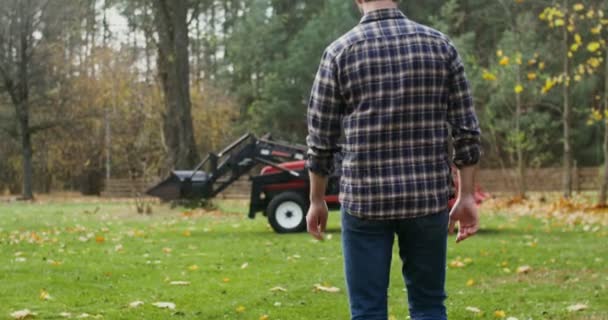 Um jovem entra em um trator, se preparando para trabalhar em campo no dia de outono — Vídeo de Stock