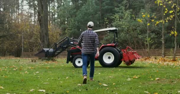 Um jovem entra em um trator, se preparando para trabalhar em campo no dia de outono — Vídeo de Stock