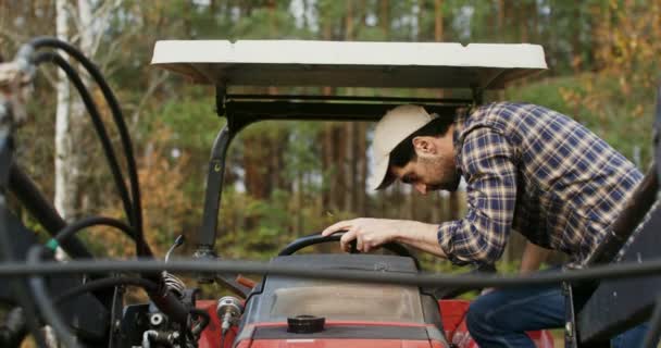 Un jeune homme monte dans un tracteur agricole, gros plan vidéo de l'avant — Video