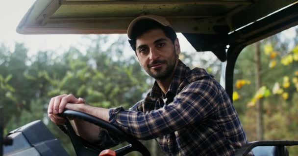 Młody człowiek uśmiecha się patrząc w kamerę siedząc w samochodzie rolniczym — Wideo stockowe