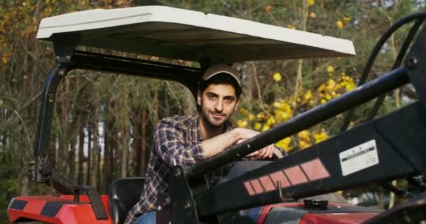Mladý muž se usmívá, dívá se do kamery, zatímco sedí v zemědělském autě — Stock video