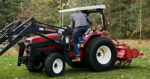 Un joven se sube a un tractor y comienza a conducir, preparándose para el trabajo — Vídeo de stock