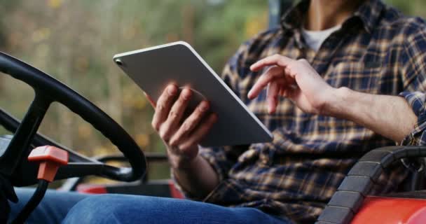 Mladý muž používá tablet, když sedí ve stojící zemědělské mašině — Stock video