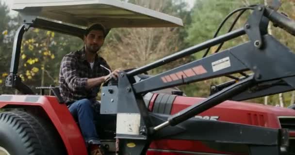 Unge man kör en liten bondgård traktor tittar på kameran i en modern gård — Stockvideo