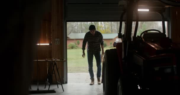 Um homem entra em uma garagem interior se aproximando de um trator — Vídeo de Stock