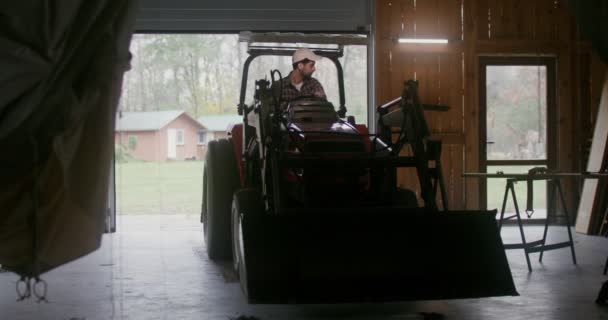 A young man starts a small agricultural tractor and drives it out of the garage — Stock Video