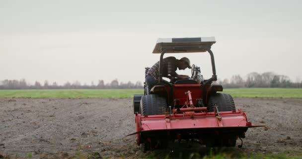 Mężczyzna wsiada za kółko ciągnika, opuszcza pług i zaczyna orać pole. — Wideo stockowe