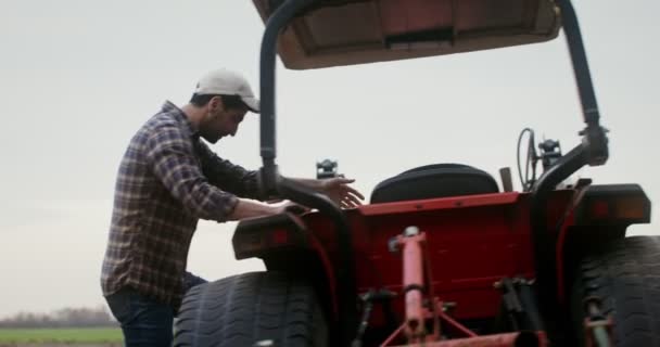 Um homem fica atrás do volante de um trator, abaixa arado e começa a arar campo — Vídeo de Stock