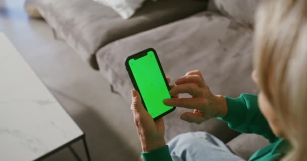 Starší žena se podívá na obrazovku mobilního telefonu, který drží — Stock video