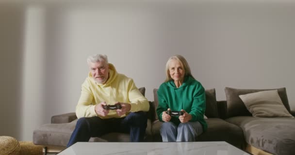 Um homem e uma mulher idosos estão jogando jogo de computador com joysticks em suas mãos — Vídeo de Stock