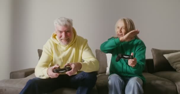 Ένας ηλικιωμένος άντρας και μια γυναίκα παίζουν ηλεκτρονικό παιχνίδι με χειριστήριο στα χέρια τους. — Αρχείο Βίντεο