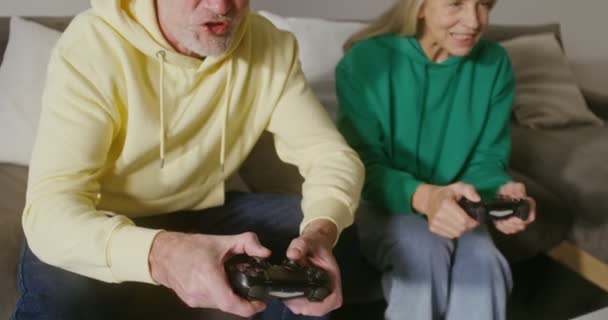 Egy idős férfi és egy nő számítógépes játékot játszanak joystickokkal a kezükben. — Stock videók