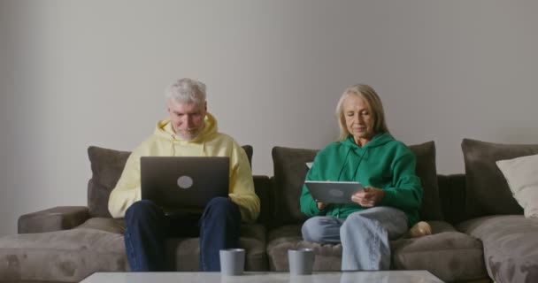 Un vecchio utilizza un computer portatile mentre seduto accanto a una donna anziana che utilizza un tablet — Video Stock