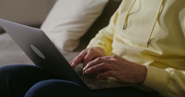 Ein älterer Mann benutzt einen Laptop, während er zu Hause auf einem Sofa sitzt — Stockvideo