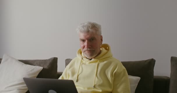 Starszy mężczyzna uśmiechający się patrząc w kamerę, patrząc w górę z pracy na laptopie — Wideo stockowe