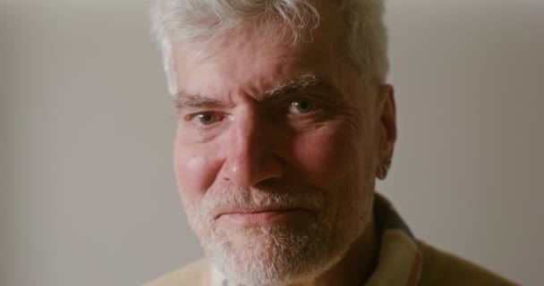 Uomo anziano con i capelli grigi e una barba sorridente guardando dritto nella fotocamera — Video Stock