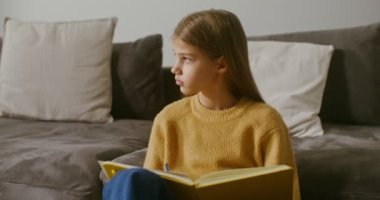 Bir kız not defterine not alıyor, evdeki kanepenin yanında oturuyor.