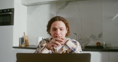 Kablosuz kulaklıklı genç adam laptoptaki bir video görüşmesinde konuşuyor.