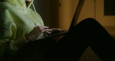 Bir kadın karanlıkta duvarın arkasında oturuyor ve dizüstü bilgisayar kullanıyor.