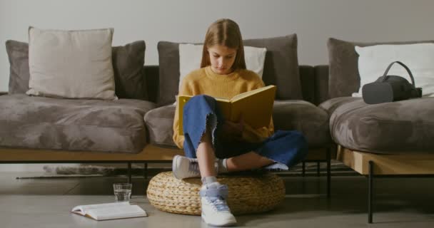 Девушка делает заметки в блокноте, сидя на полу рядом с диваном дома — стоковое видео