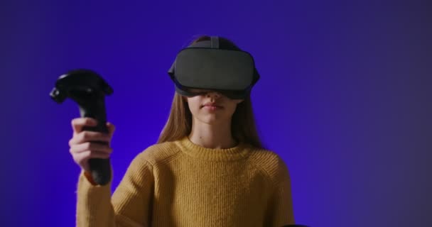 Uma menina em óculos de realidade virtual joga um jogo online, fazendo movimentos de mão — Vídeo de Stock