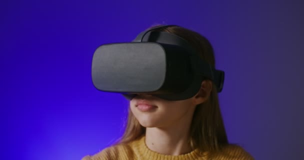 Uma menina em óculos de realidade virtual joga um jogo online, fazendo movimentos de mão — Vídeo de Stock