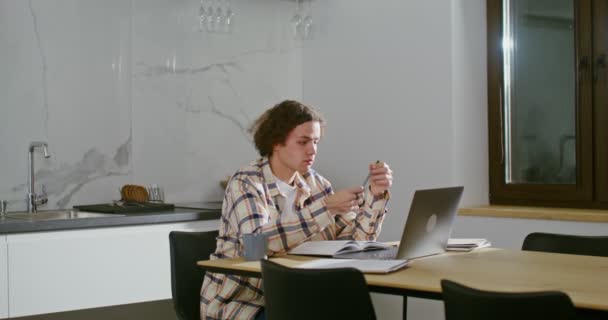 Νεαρός στη σκέψη, κάθεται μπροστά από ανοιχτά βιβλία και ένα φορητό υπολογιστή στο τραπέζι — Αρχείο Βίντεο