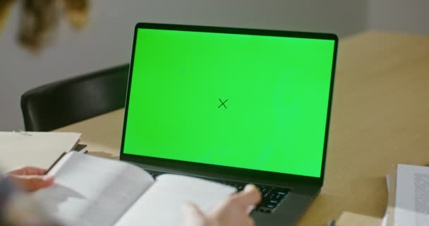 Mężczyzna przegląda książkę siedząc przed zielonym ekranem laptopa. — Wideo stockowe