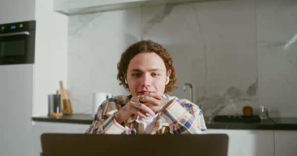 Hombre joven con auriculares inalámbricos está hablando en una videollamada en un ordenador portátil — Vídeo de stock