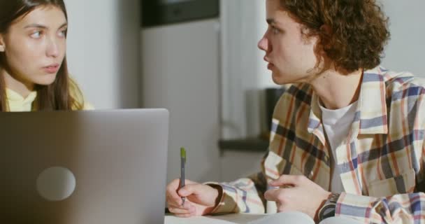 Pareja joven se dedican en casa con libros y un ordenador portátil abierto — Vídeos de Stock