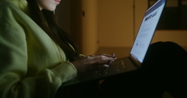 A woman sits in the darkness on the floor in back against wall and uses a laptop — Stock Video