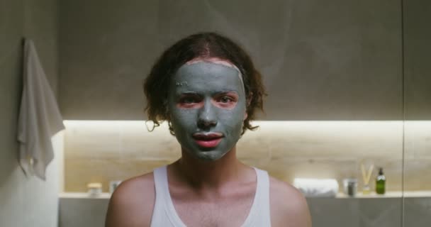 Jeune homme avec un masque d'argile sur le visage souriant en regardant dans la caméra — Video