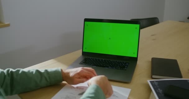 Un hombre está trabajando en un dibujo, sentado frente a un portátil con una pantalla verde — Vídeos de Stock