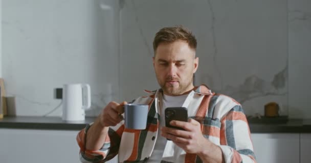 Jongeman drinkt koffie zonder zijn ogen van het scherm van een mobiele telefoon te halen — Stockvideo