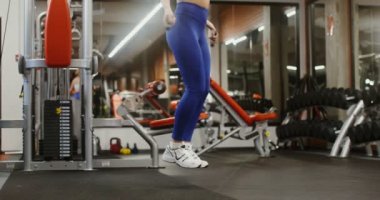 Genç bir kadın ip atlıyor, modern bir spor salonunda tek başına.