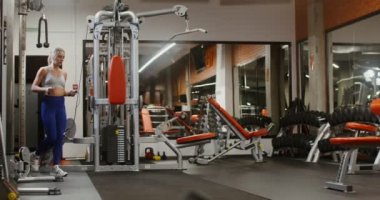 Genç bir kadın ip atlıyor, modern bir spor salonunda tek başına.