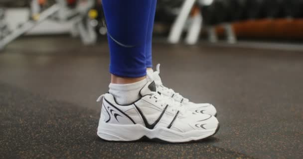 Ноги женщины в кроссовках, прыгающей верёвкой в спортзале, крупным планом — стоковое видео