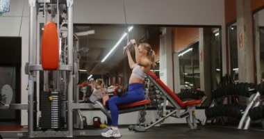 Beden eğitiminde egzersiz makinesini kullanarak sırt kası egzersizi yapan genç bir kadın.