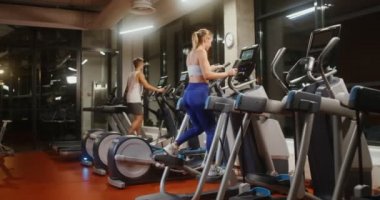 Gençler kapalı bir spor salonunda elips üzerinde egzersiz yapıyorlar.