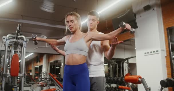 A woman lifting small dumbbells under the guidance of a young trainer — Stock videók