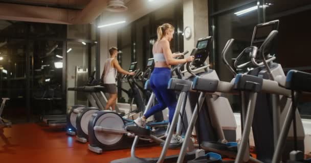 Los jóvenes hacen ejercicio en una elipse en un gimnasio cubierto bien equipado — Vídeo de stock