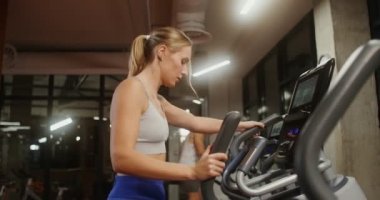 Gençler kapalı bir spor salonunda elips üzerinde egzersiz yapıyorlar.