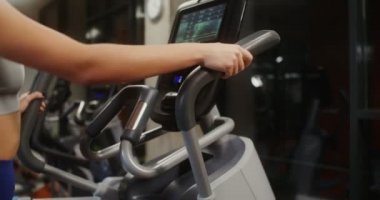 Bir kadın kapalı spor salonunda bir elips içinde, yakın çekim yan görüntü videosu çekiyor.