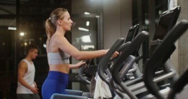 Gençler kapalı bir spor salonunda elips üzerinde egzersiz yapıyorlar.