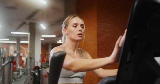 A woman is engaged in an ellipse in an indoor gym, Close-up — ストック動画