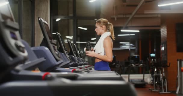 Mladá žena začne trénovat na běžeckém pásu, zvolí si tréninkový režim a rychlost — Stock video